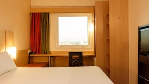 Een hotelkamer met een bed, bureau, stoel, televisie en raam met gordijnen.