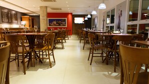 Ein geräumiges Restaurant mit Holztischen und -stühlen, einer roten Akzentwand und einem Fernsehbildschirm.