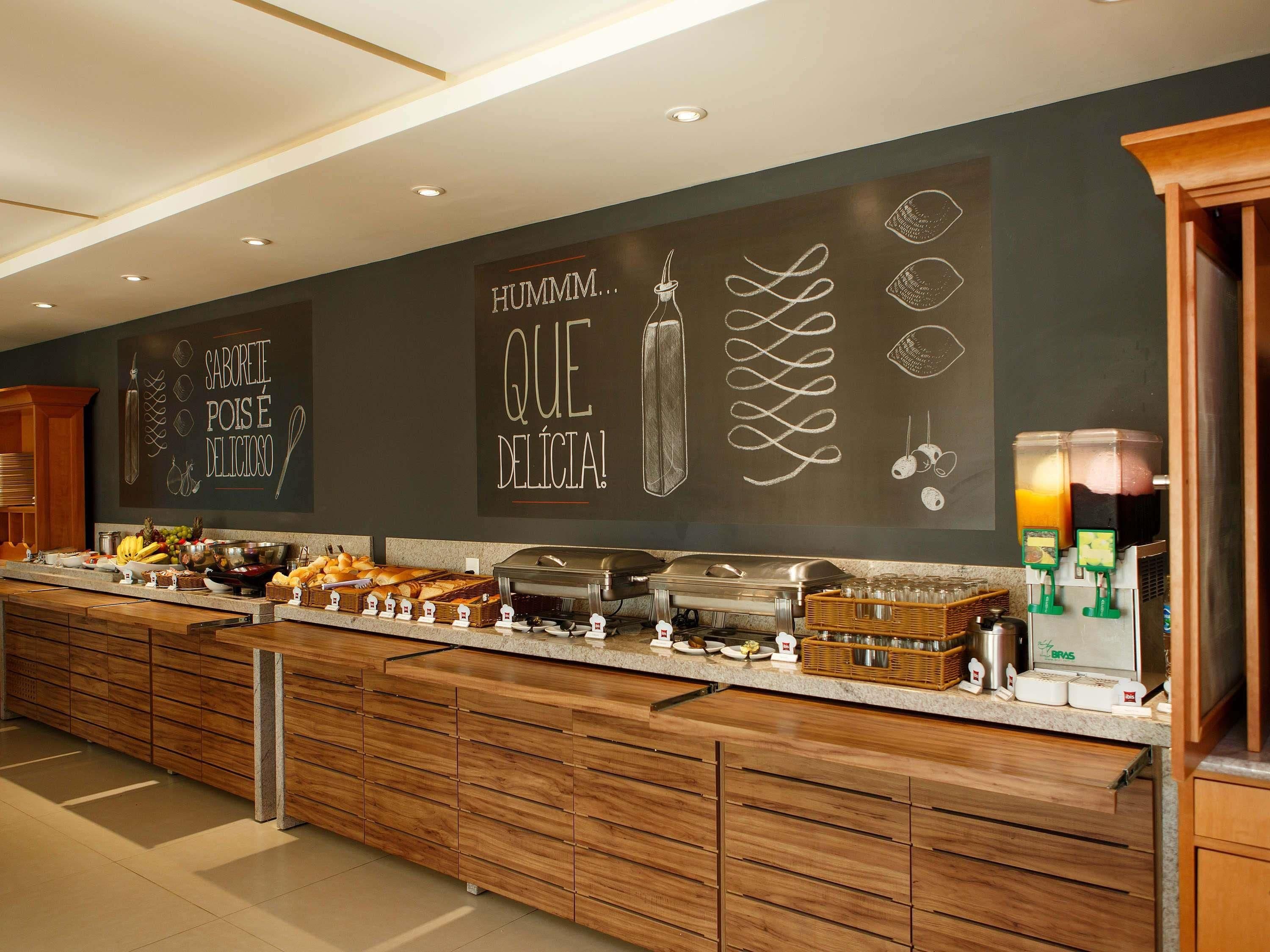 A buffet area with a chalkboard wall displaying food-related text and drawings, a buffet counter with various food items, and a juice dispenser.