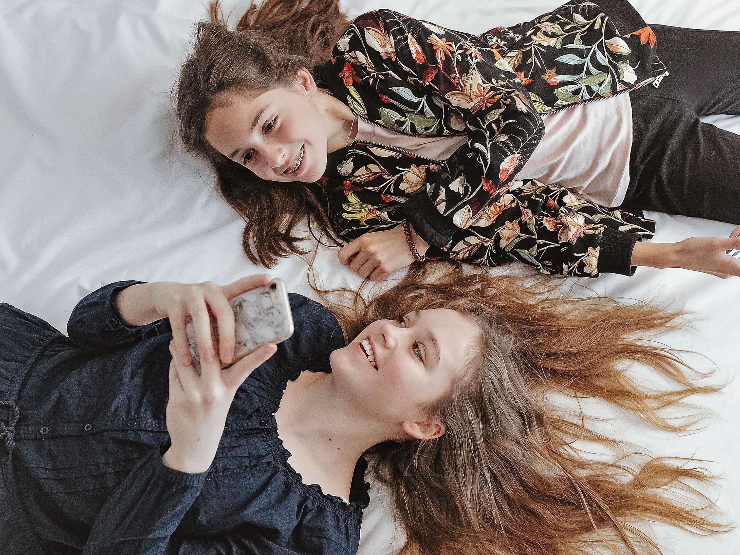 Two people lying on a bed, one holding a smartphone.
