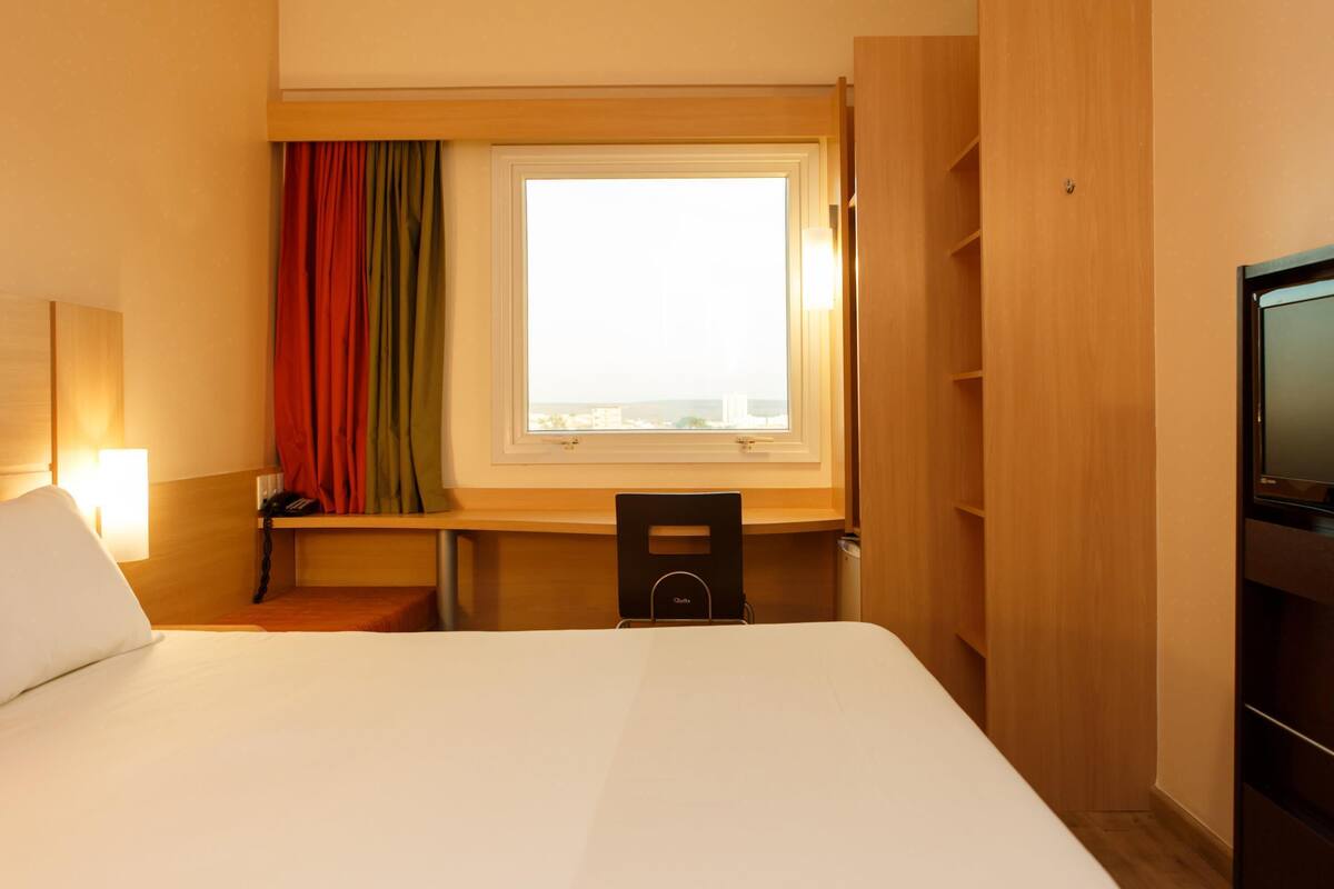Een hotelkamer met een bed, bureau, stoel, televisie en raam met gordijnen.