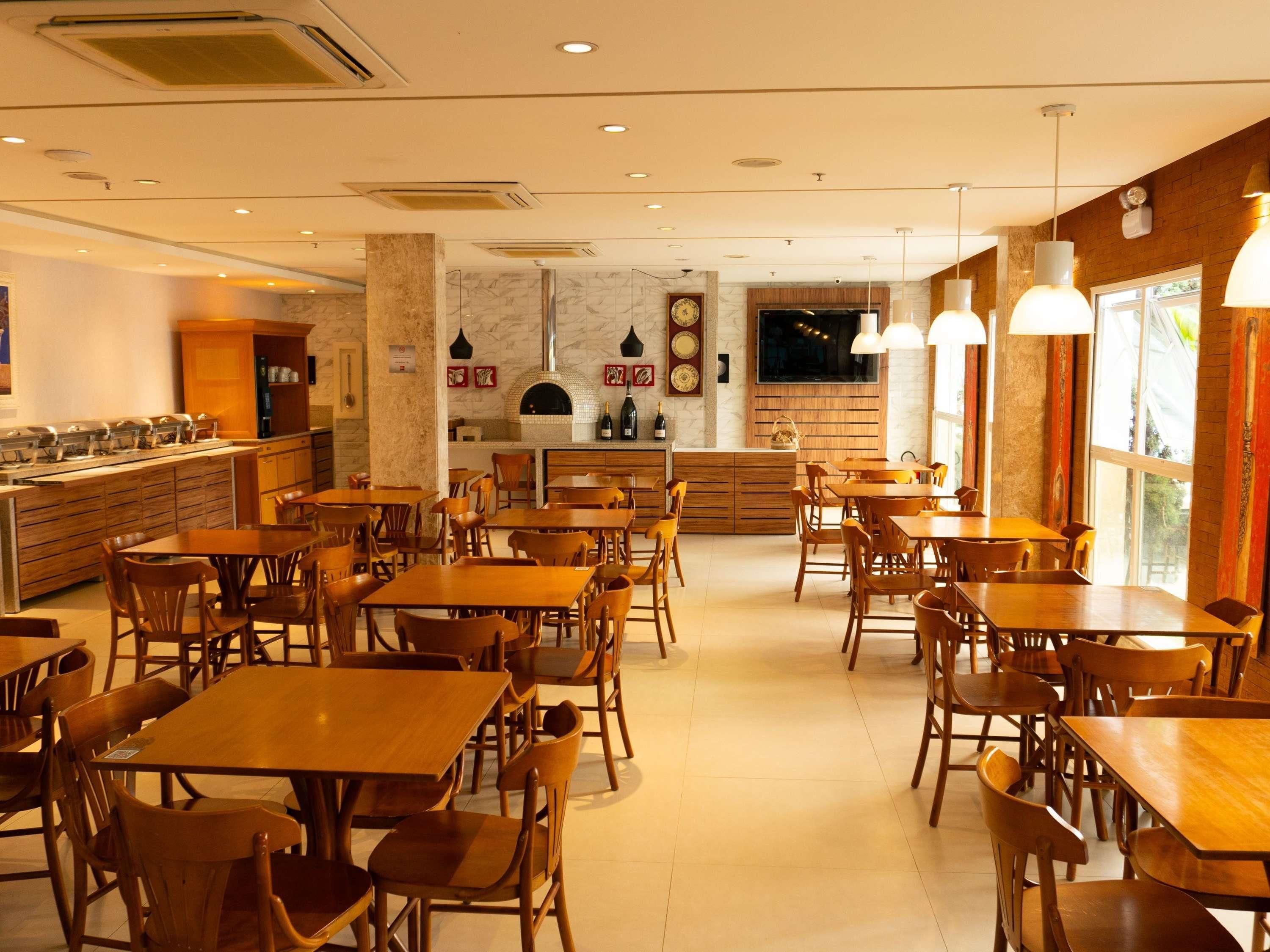 Un restaurante con mesas y sillas de madera, una zona de cocina y un ventanal grande.