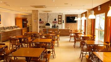 Un restaurante con mesas y sillas de madera, una zona de cocina y un ventanal grande.