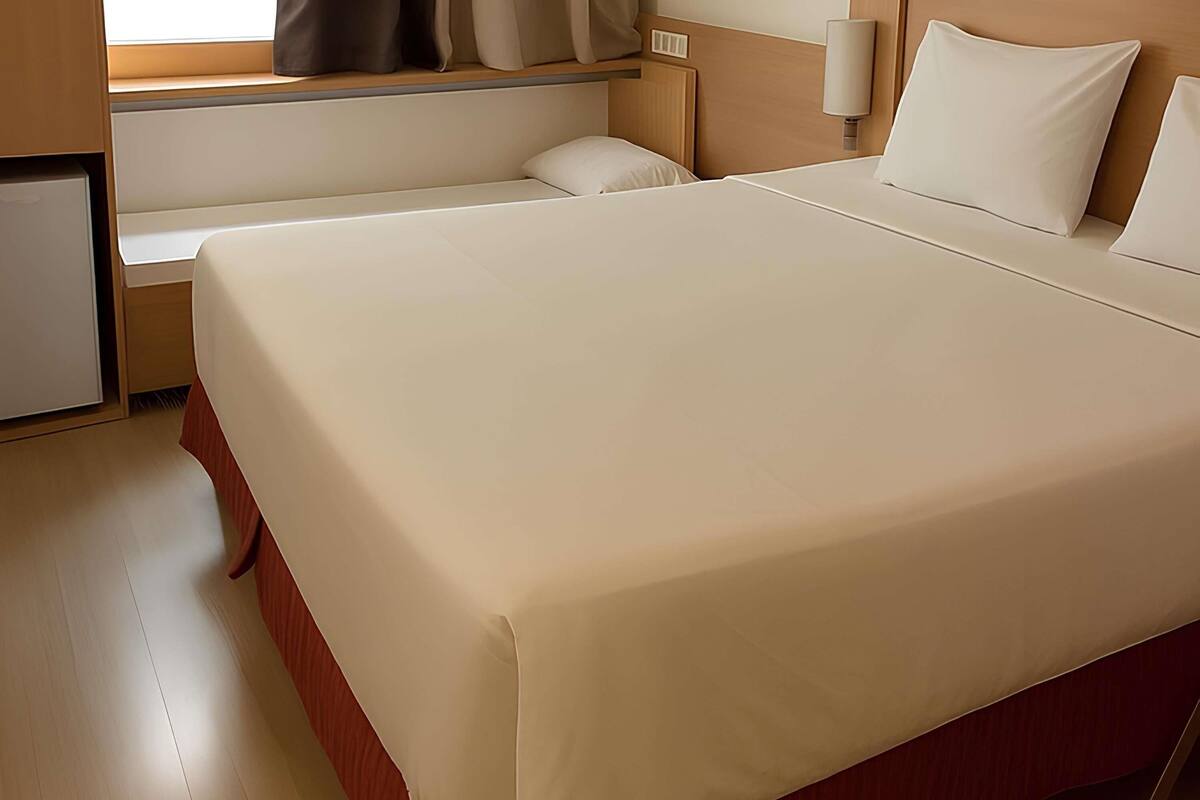 Een hotelkamer met een groot bed, een nachtkastje, een lamp en een raam met gordijnen.