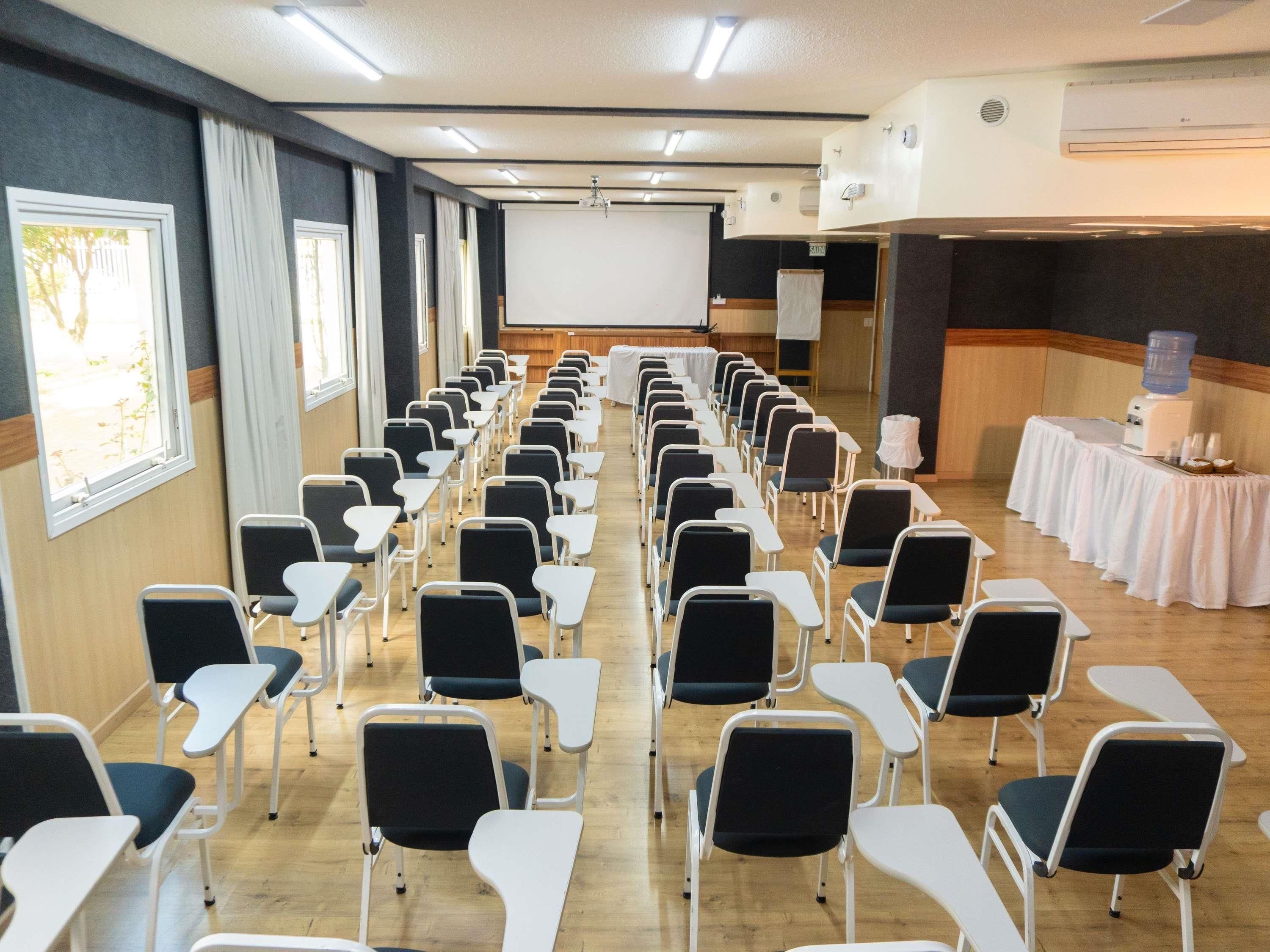 A conference room with rows of chairs, a projector screen, and a water dispenser.
