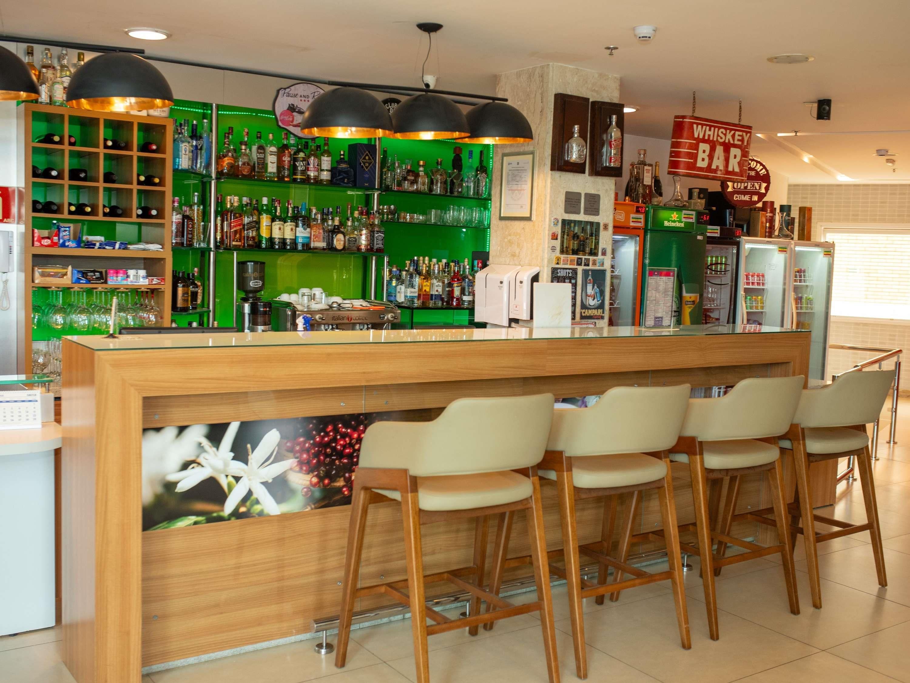 A bar area with a green backdrop, a whiskey bar sign, and a variety of liquor bottles.