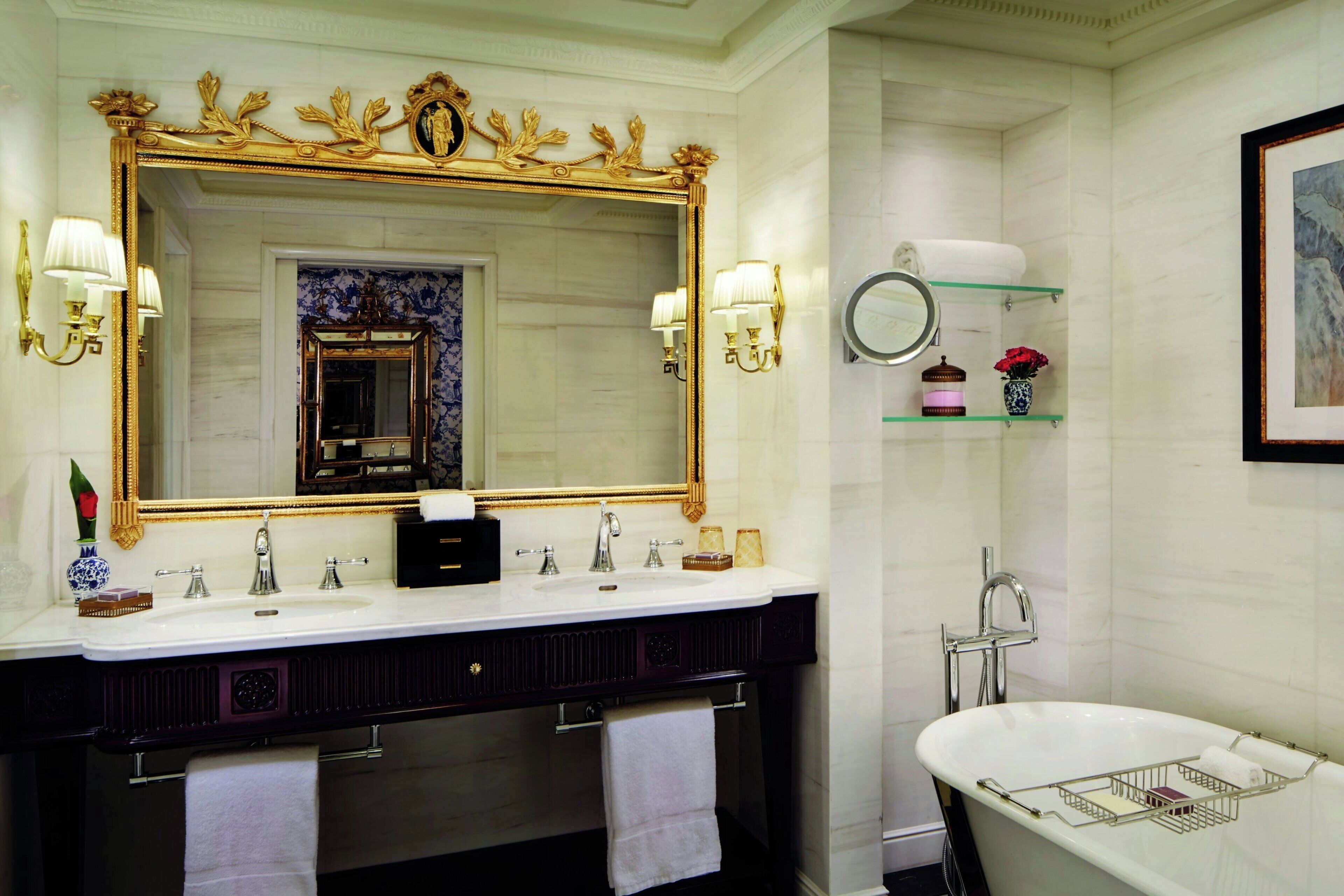 A bathroom with a large mirror, a bathtub, a vanity with a sink, and a shelf with toiletries.
