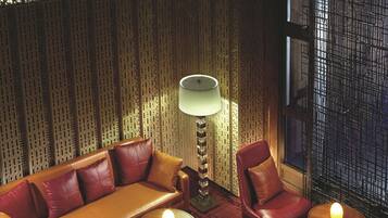 A room with a patterned wall, a sofa, chairs, and small tables with lamps.