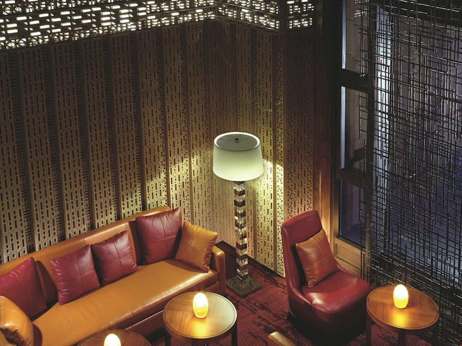 A room with a patterned wall, a sofa, chairs, and small tables with lamps.