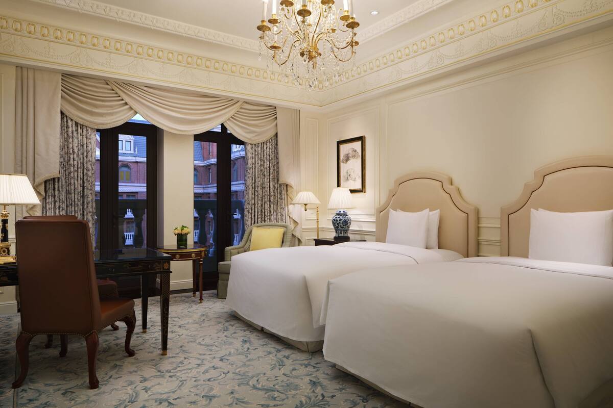 A hotel room with two beds, a desk, a chair, and a chandelier.