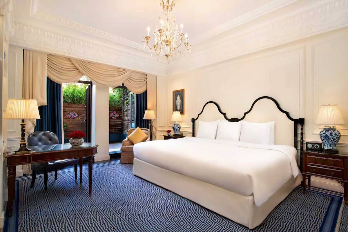 A luxurious hotel room with a large bed, a desk, a chair, and a chandelier.