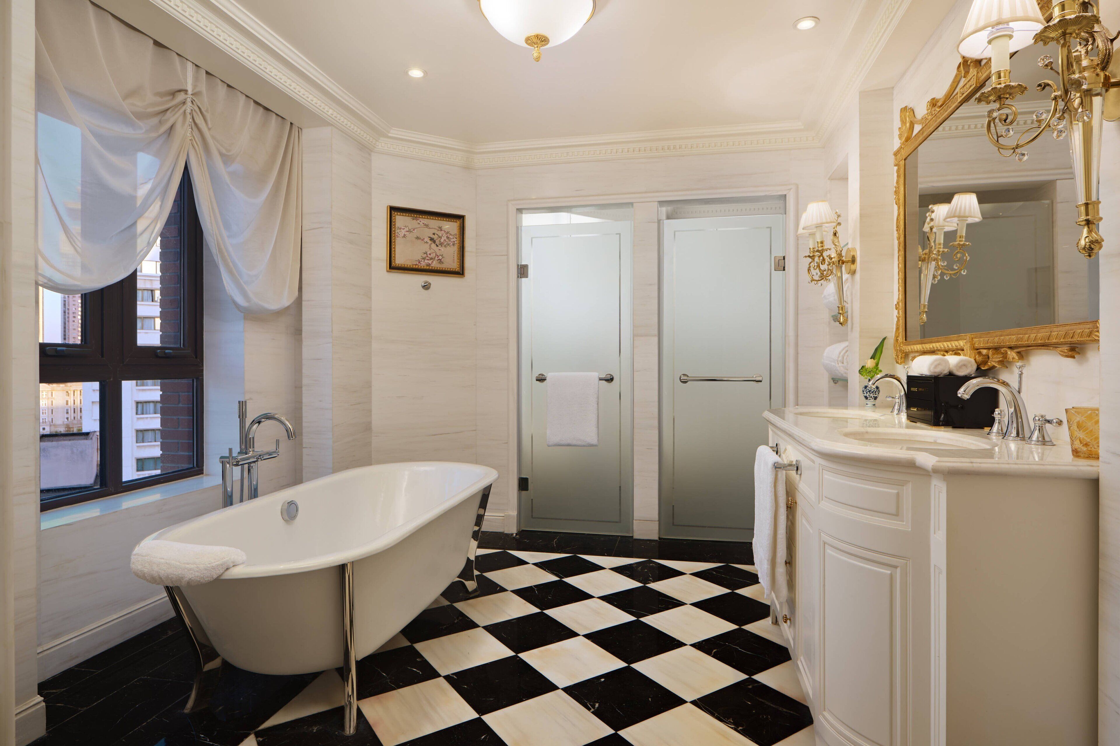 A bathroom with a freestanding bathtub, a double vanity with a large mirror, and a checkered floor.
