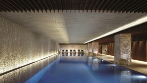 A modern indoor swimming pool with a wooden floor, stone walls, and a long bench along one side. - The Ritz-Carlton, Tianjin (Tianjin)