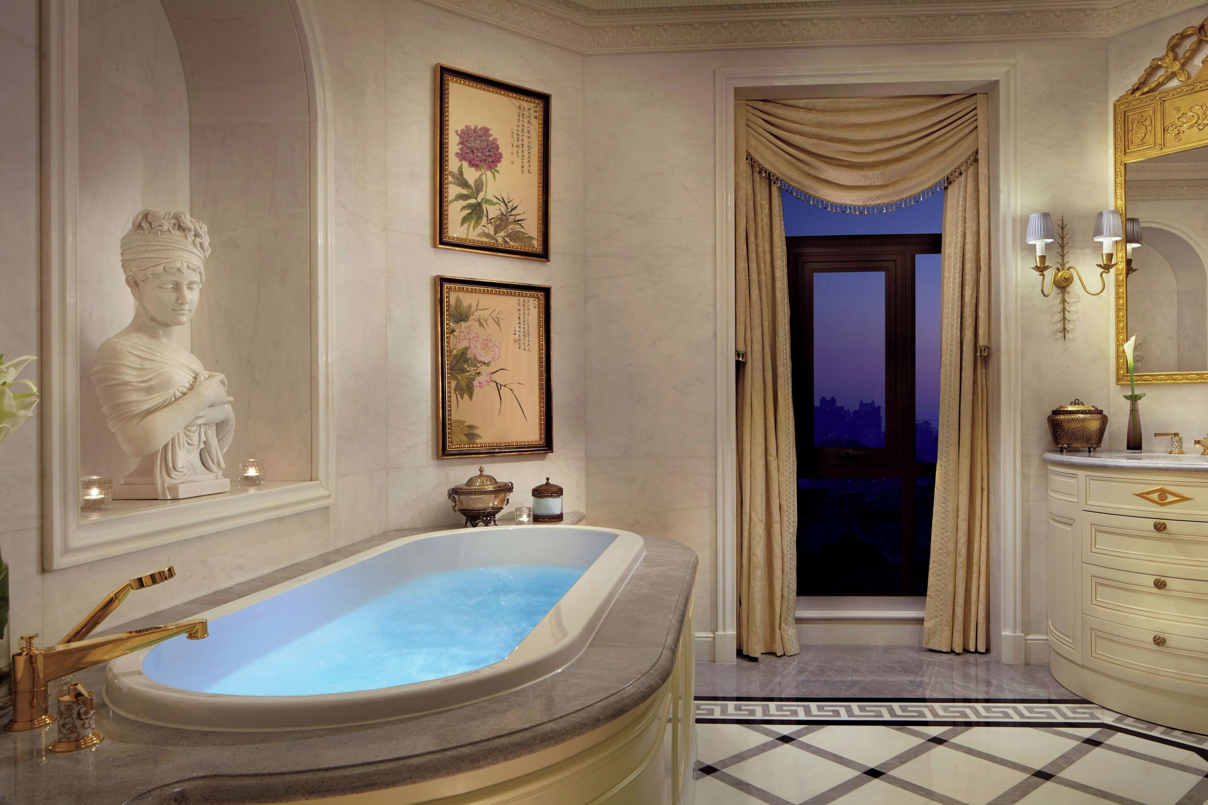 A luxurious bathroom with a freestanding bathtub, marble flooring, and classical decor including a bust sculpture and framed calligraphy.