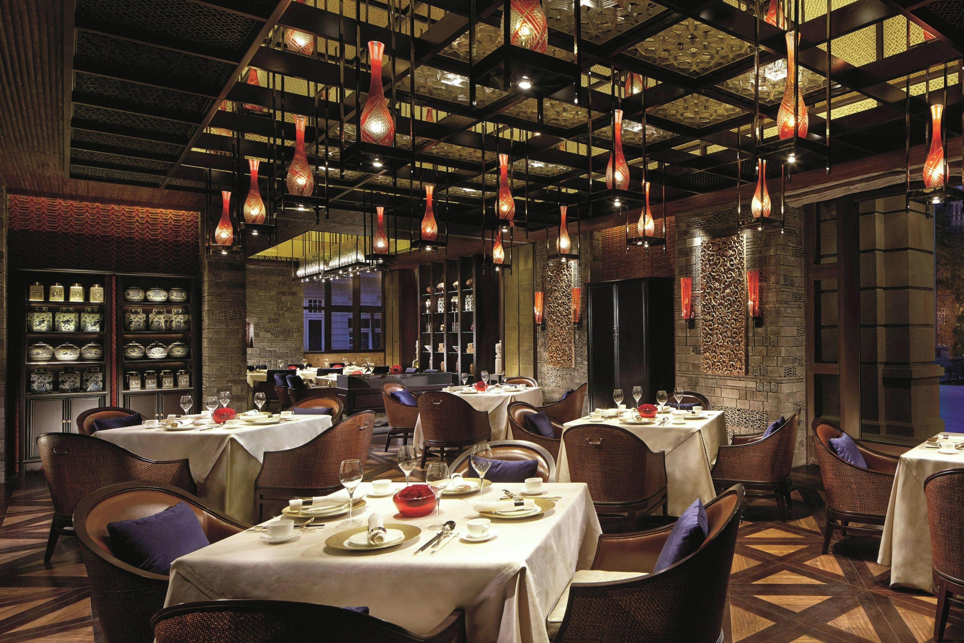 Interior de restaurante con varias mesas, sillas, lámparas colgantes y elementos decorativos en las paredes.