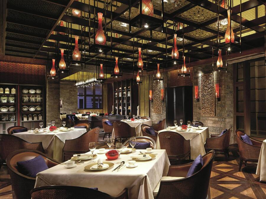 Interior de restaurante con varias mesas, sillas, lámparas colgantes y elementos decorativos en las paredes.