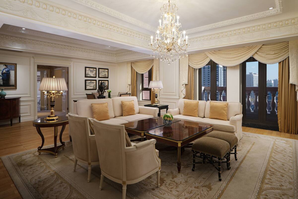 A spacious living room with a large sofa, armchairs, a coffee table, and a chandelier.