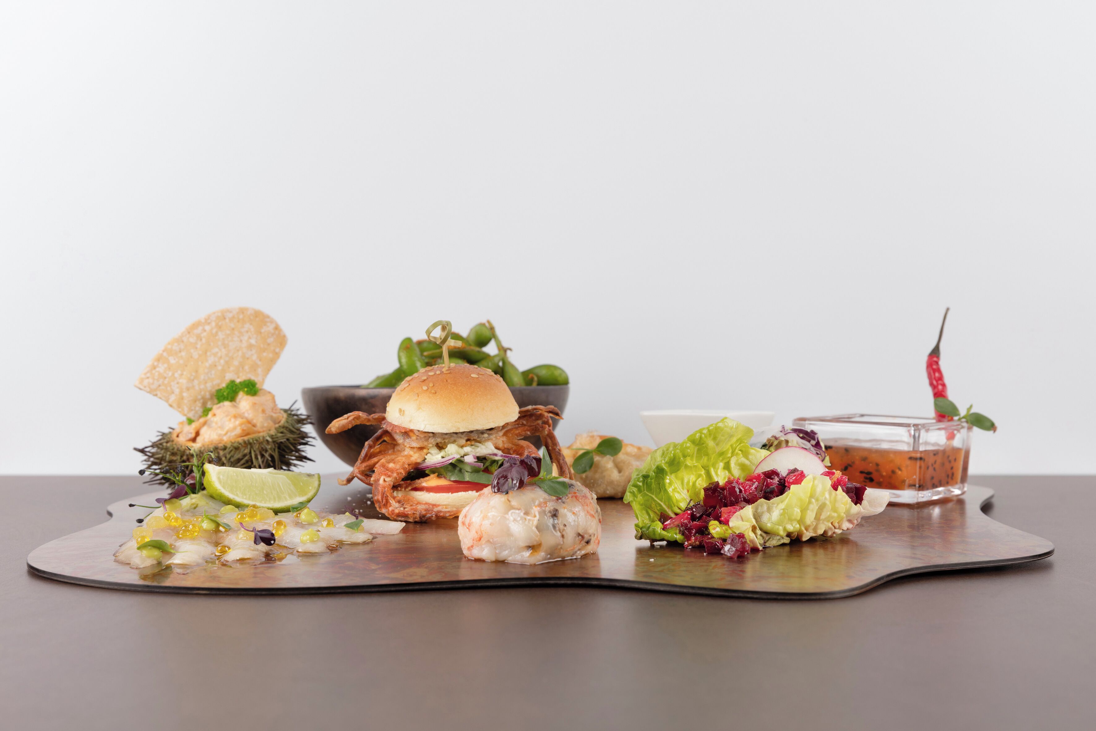 Verschiedene Gerichte, darunter ein Burger, Meeresfrüchte und ein Salat, auf einer Metallplatte.