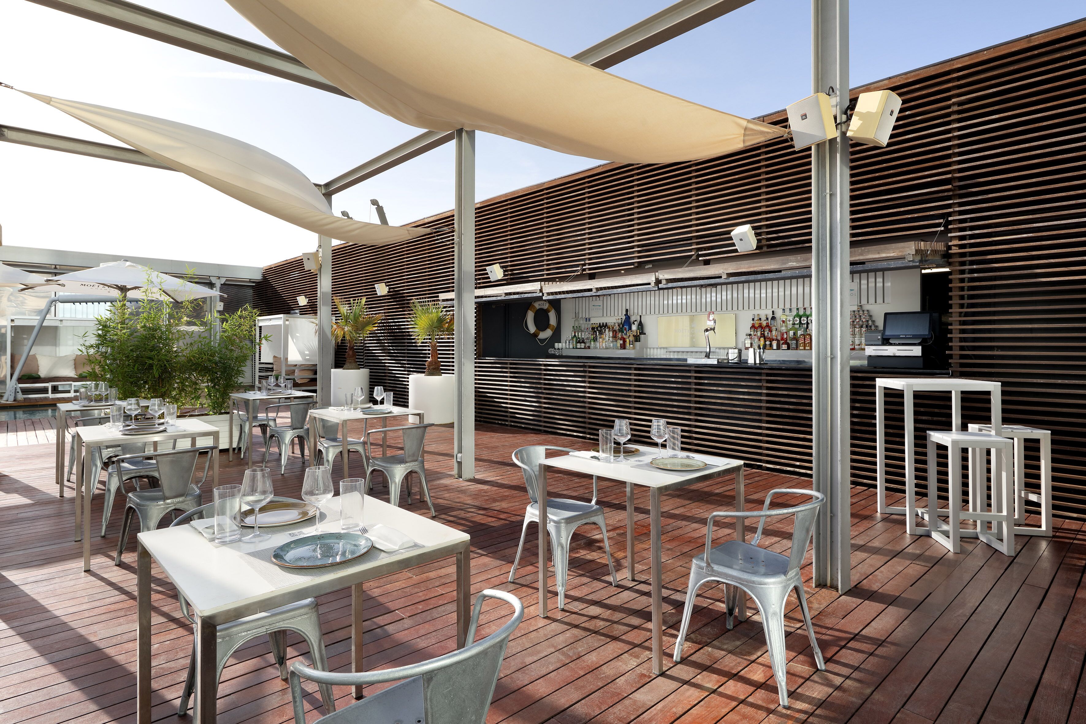 An outdoor dining area with tables and chairs, a bar with bottles, and a lifebuoy on the wall.