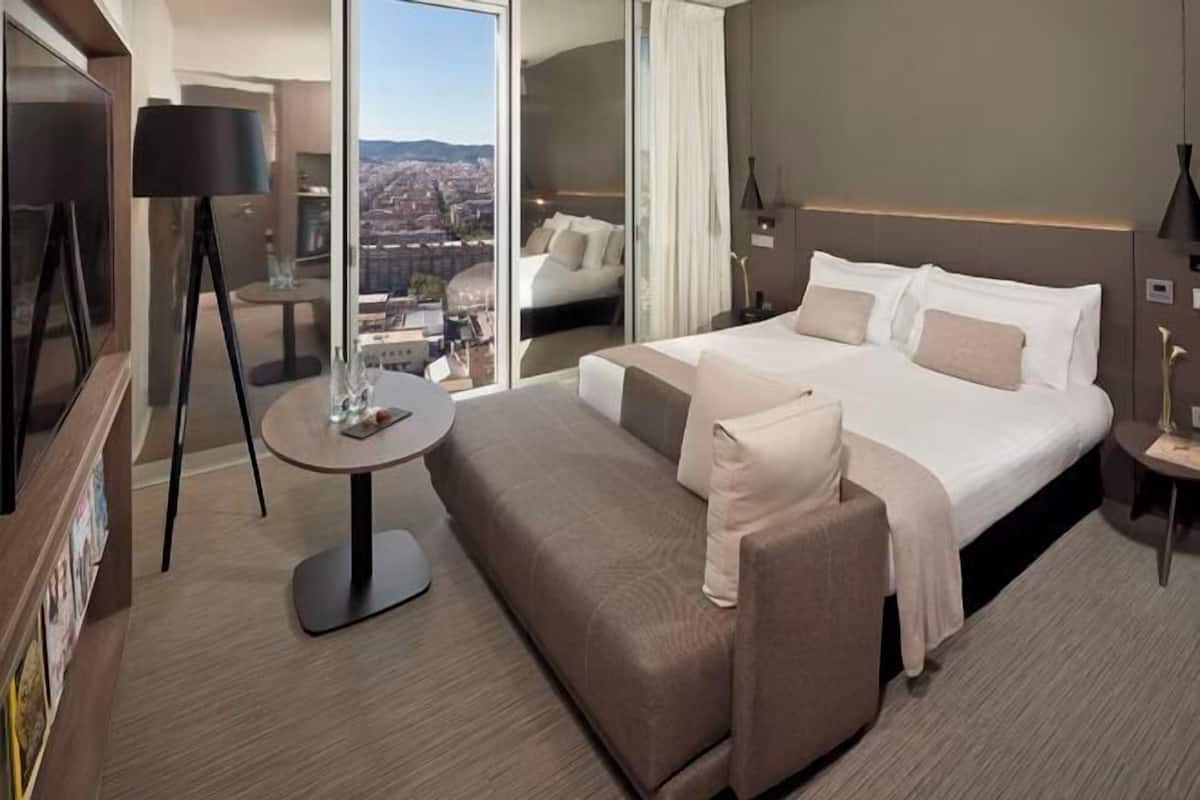 A modern hotel room with a large bed, a sofa, a small table, and a TV.