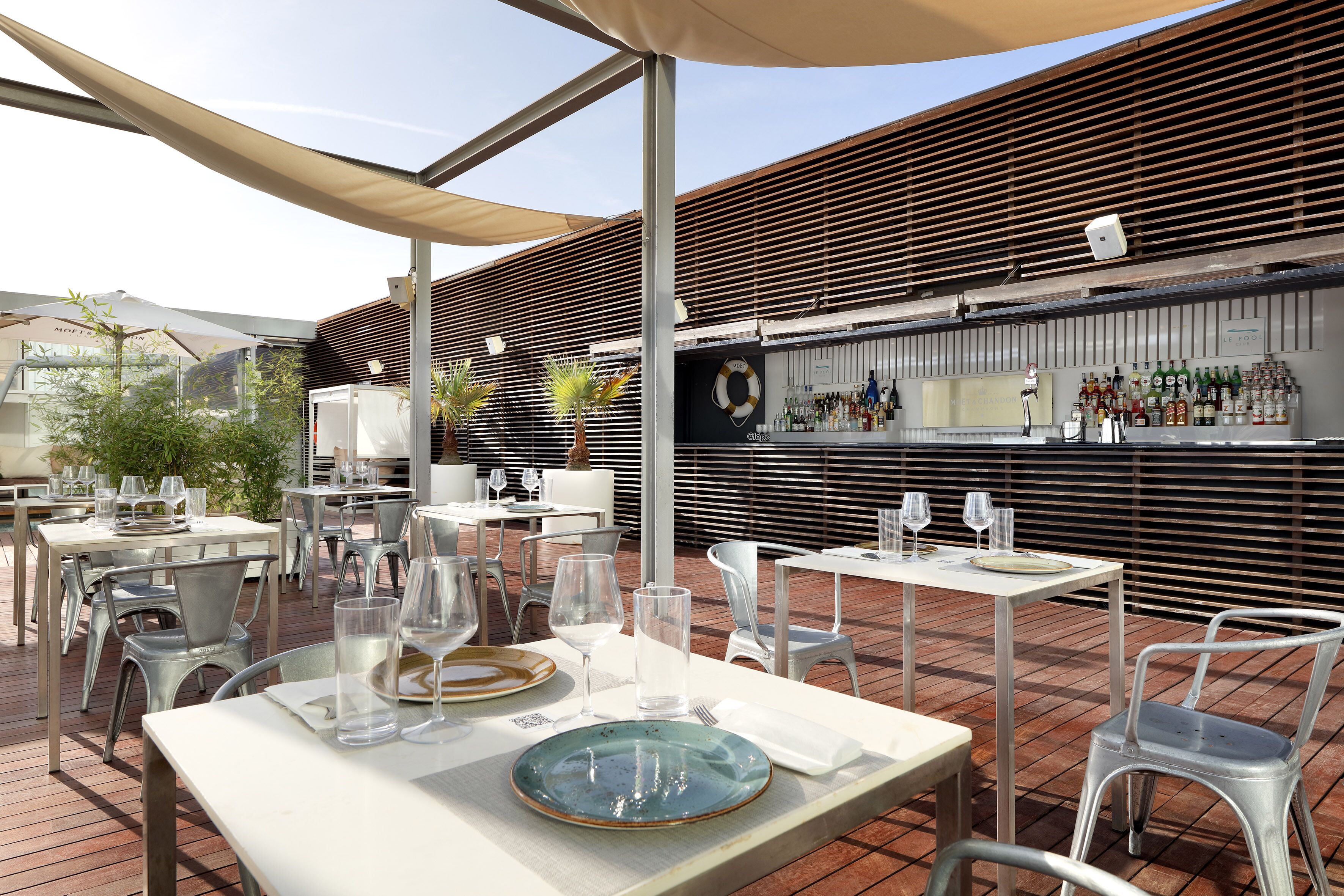 Un área de comedor al aire libre con mesas y sillas, una barra con botellas y una decoración de boya salvavidas.