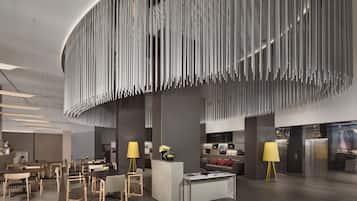 Un moderno vestíbulo de hotel con un mostrador de recepción central, zona de estar y un diseño de techo único.