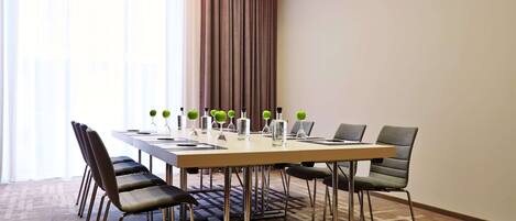 A conference room with a long table, six chairs, and a large window with curtains.