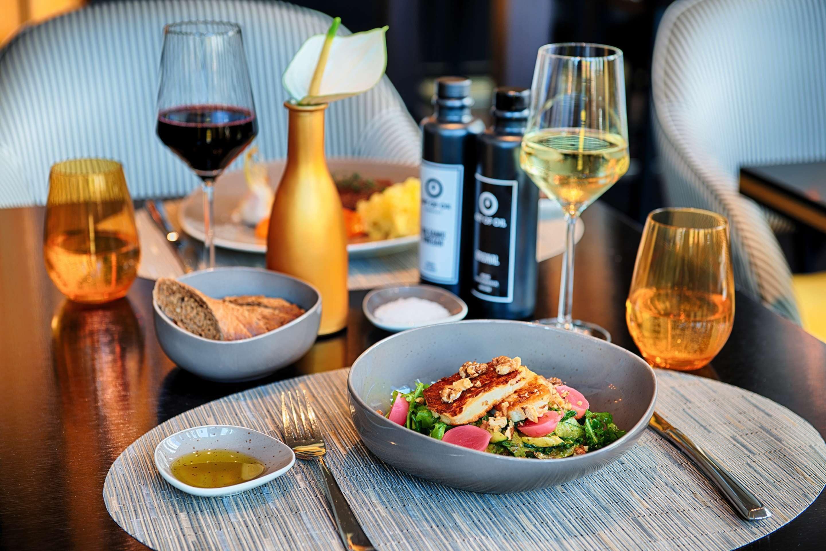 Una mesa de comedor con comida, copas de vino y condimentos.