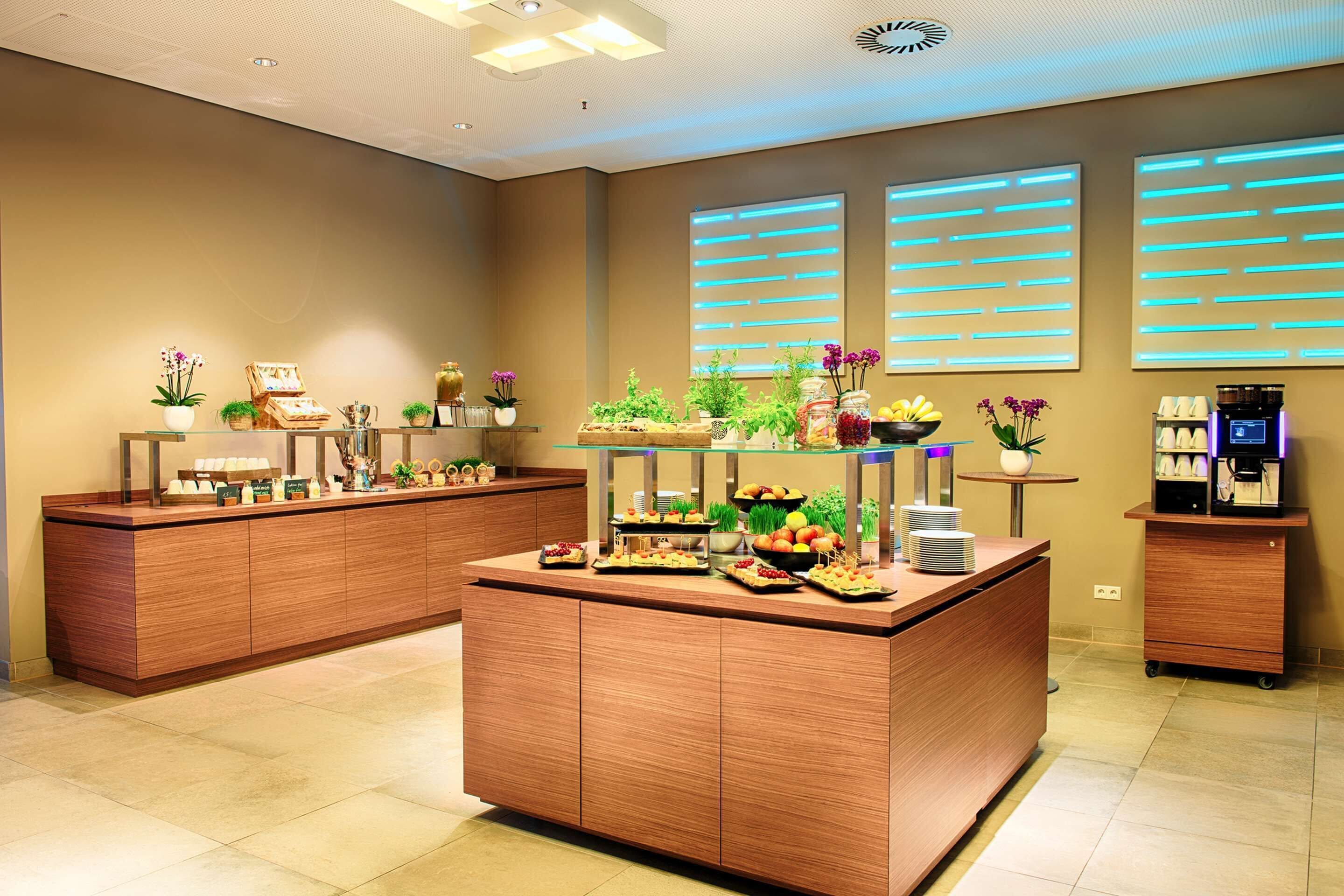 Ein Hotel-Empfangsbereich mit einem Holzbüro, einer Kaffeemaschine und verschiedenen Dekorationselementen, darunter Pflanzen und gerahmte Bilder.