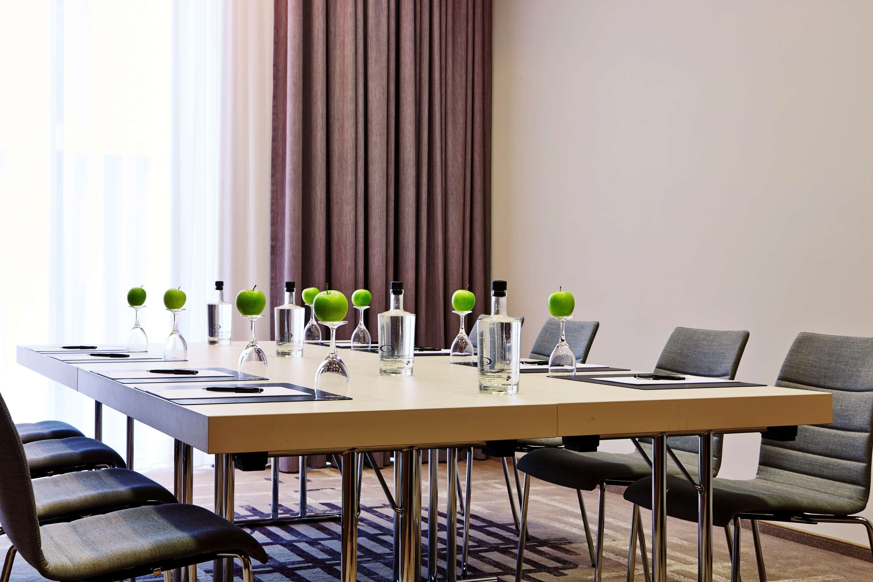 Un salón de conferencias con una mesa larga, sillas y objetos decorativos, incluyendo manzanas verdes y botellas.