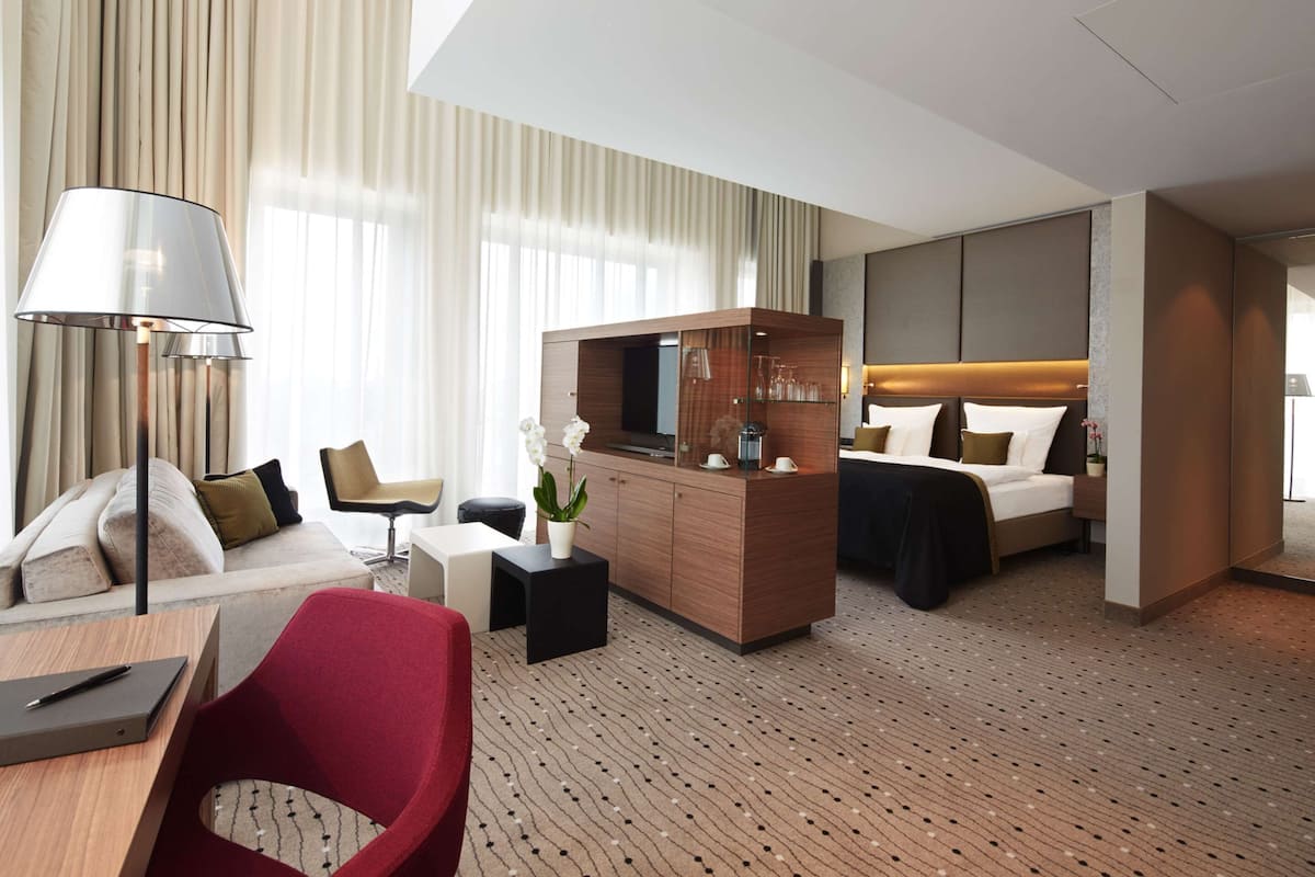 A modern hotel room with a bed, a desk, a chair, a TV, and a large window with curtains.