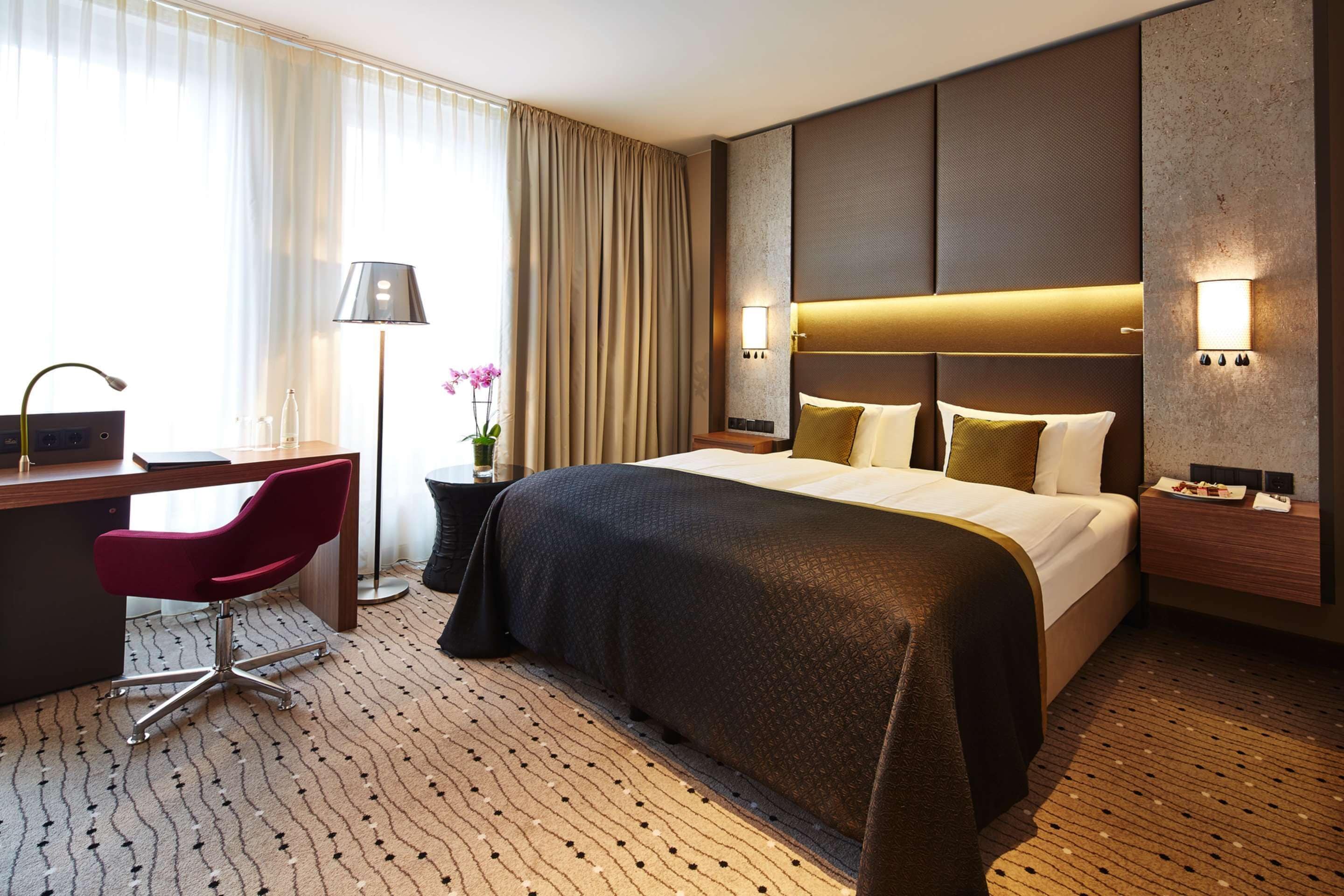 Ein Hotelzimmer mit einem großen Bett, einem Schreibtisch mit Stuhl, einer Lampe und einem Nachttisch mit Lampe.