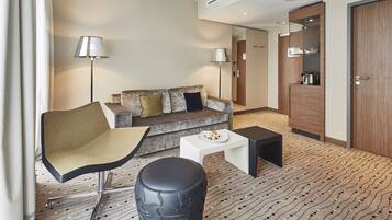 Una habitación de hotel moderna con un sofá, una silla, una mesita con un plato de comida y una cafetera.