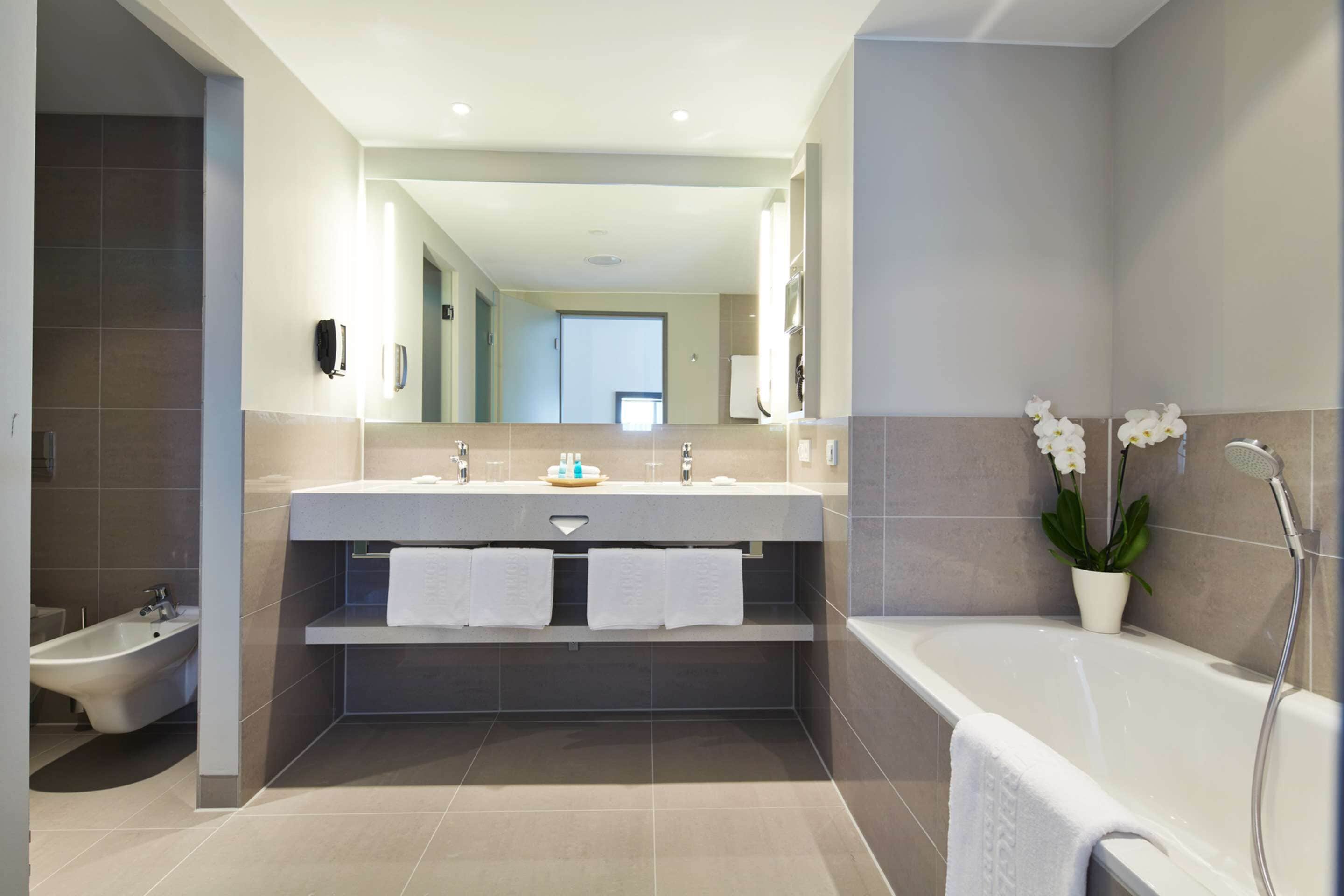 A modern bathroom with a bidet, a bathtub, and a large mirror above a vanity with two sinks.