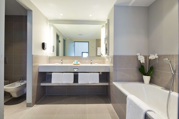 A modern bathroom with a bidet, a bathtub, and a large mirror above a vanity with two sinks.