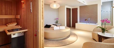 A modern spa room with a wooden sauna, a round seating area with a small table, and a large mirror.