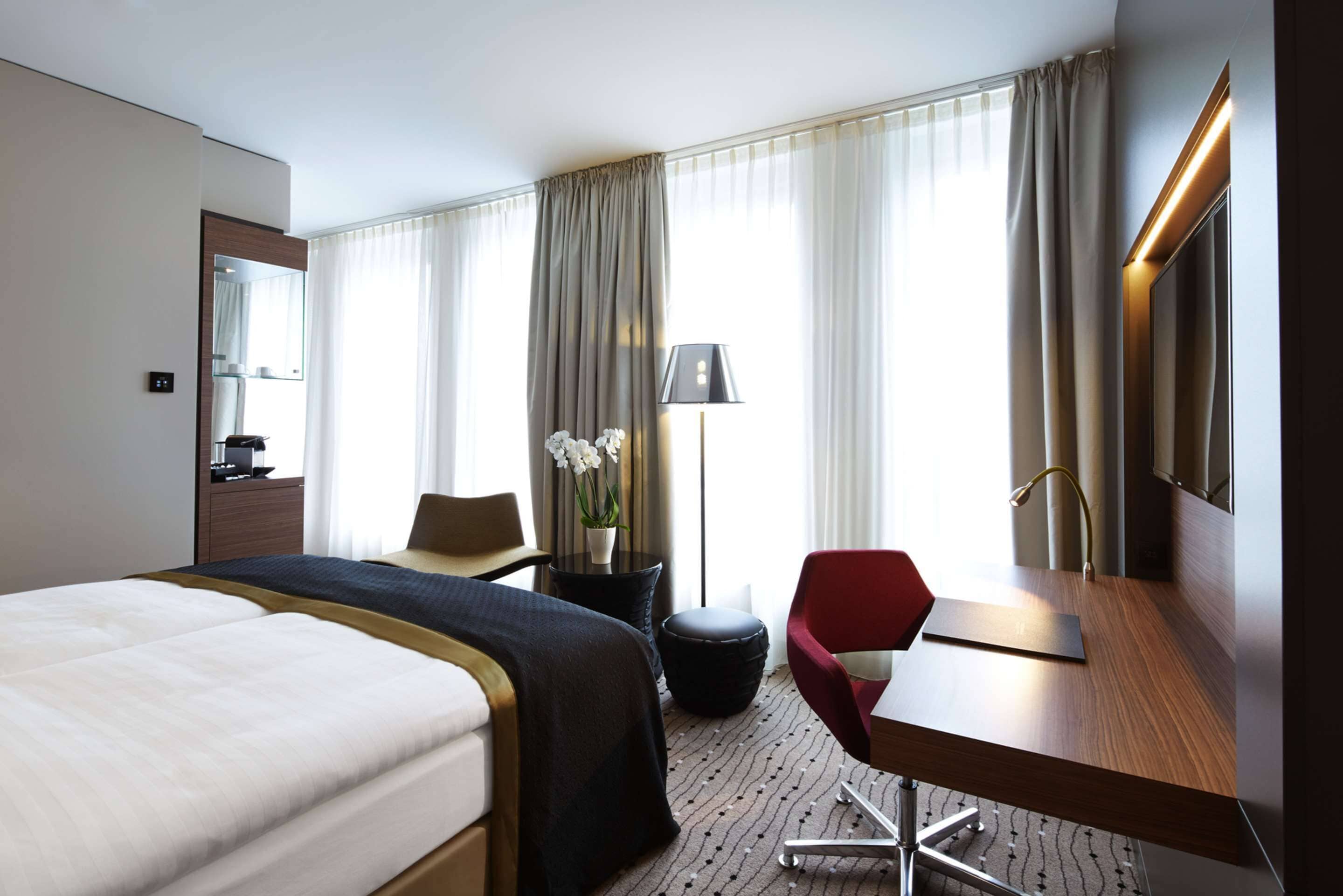 Habitació d'hotel amb un llit gran, una escriptori amb una cadira, una taula petita amb una làmpada i un mirall a la paret.