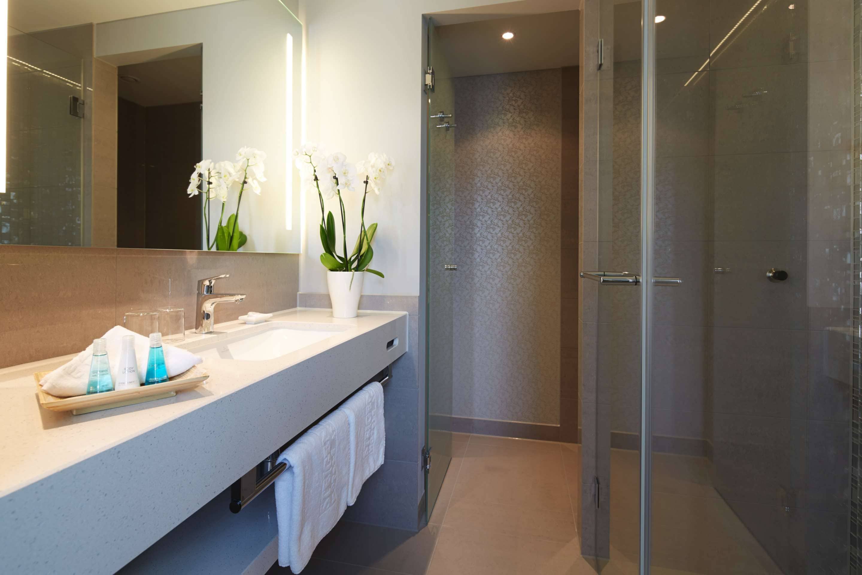 Un baño moderno con cabina de ducha de vidrio, un espejo grande y un lavabo blanco con artículos de aseo.