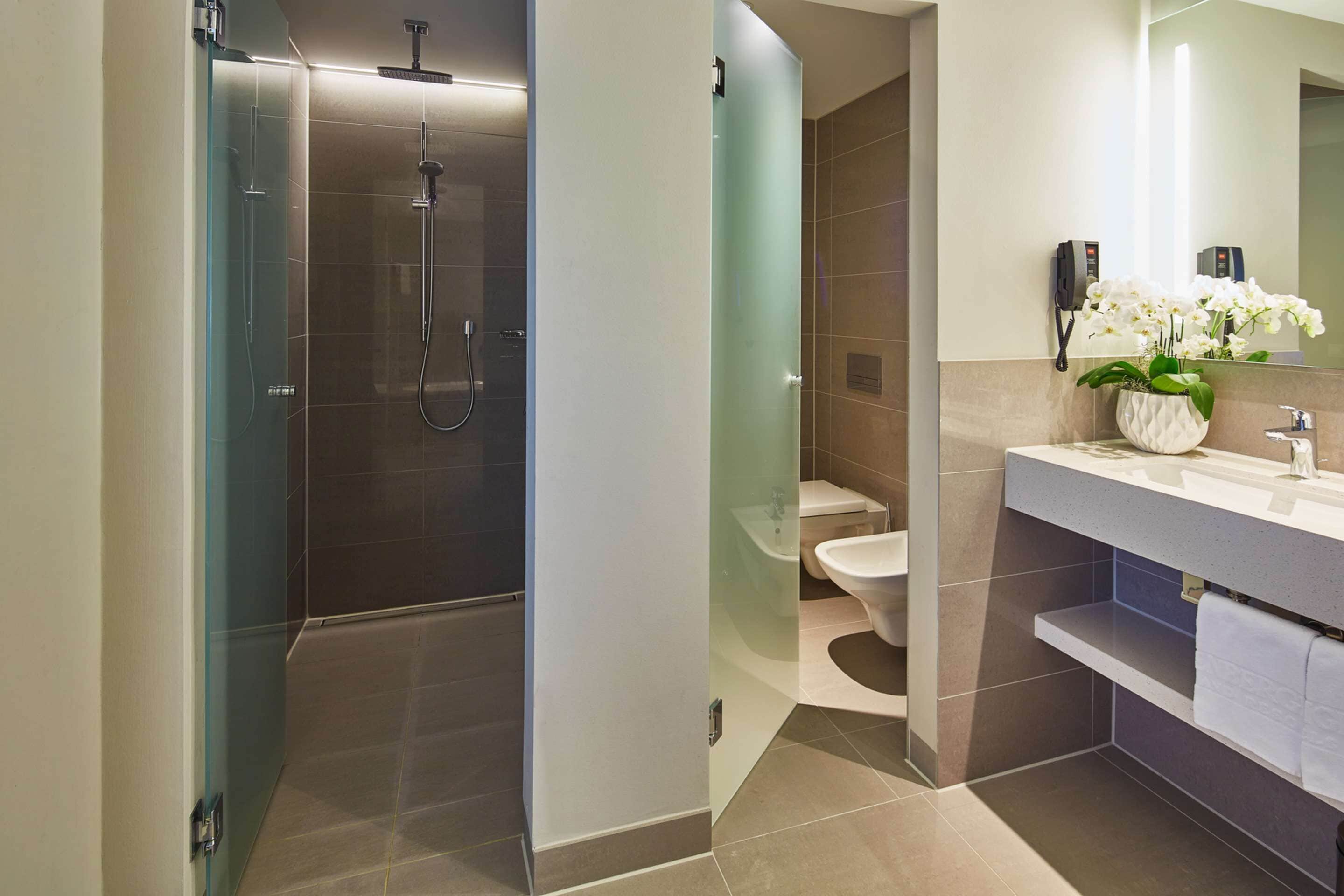 A modern bathroom with a glass-enclosed shower, a toilet, and a vanity with a mirror and a plant.