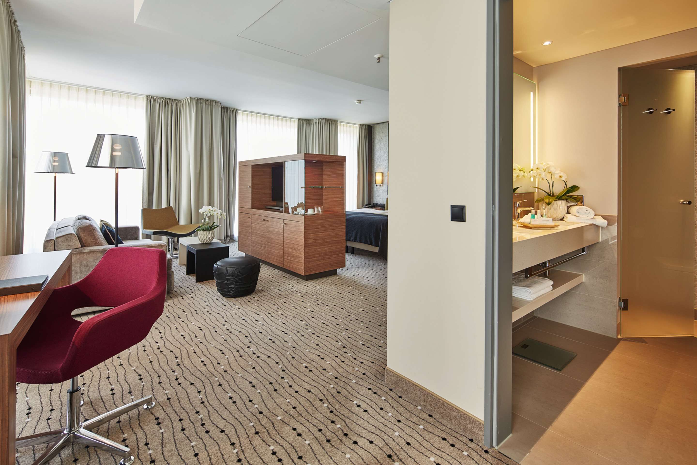 Habitación de hotel con escritorio, silla roja, cómoda de madera y un espejo grande.