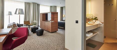 A hotel room with a desk, red chair, wooden dresser, and a large mirror.