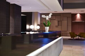 A modern reception area with a dark reception desk, a white vase with white flowers, and yellow chairs. - Steigenberger Hotel Am Kanzleramt (Berlin)