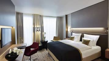 Una habitación de hotel moderna con una cama grande, un escritorio con silla, un televisor y un jarrón decorativo.
