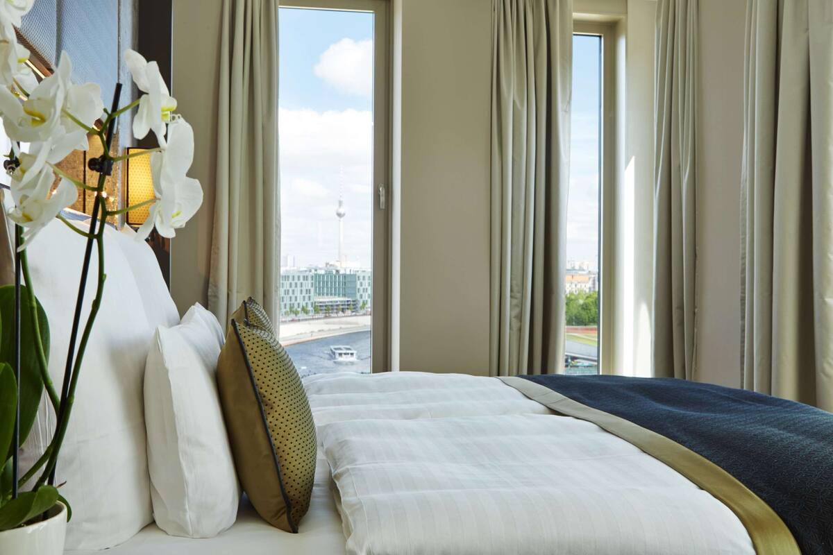 A hotel room with a bed, a potted plant, and a view of a cityscape.