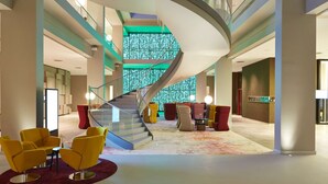 A modern lobby with a spiral staircase, yellow armchairs, and a colorful carpet. - Steigenberger Hotel Am Kanzleramt (Berlin)