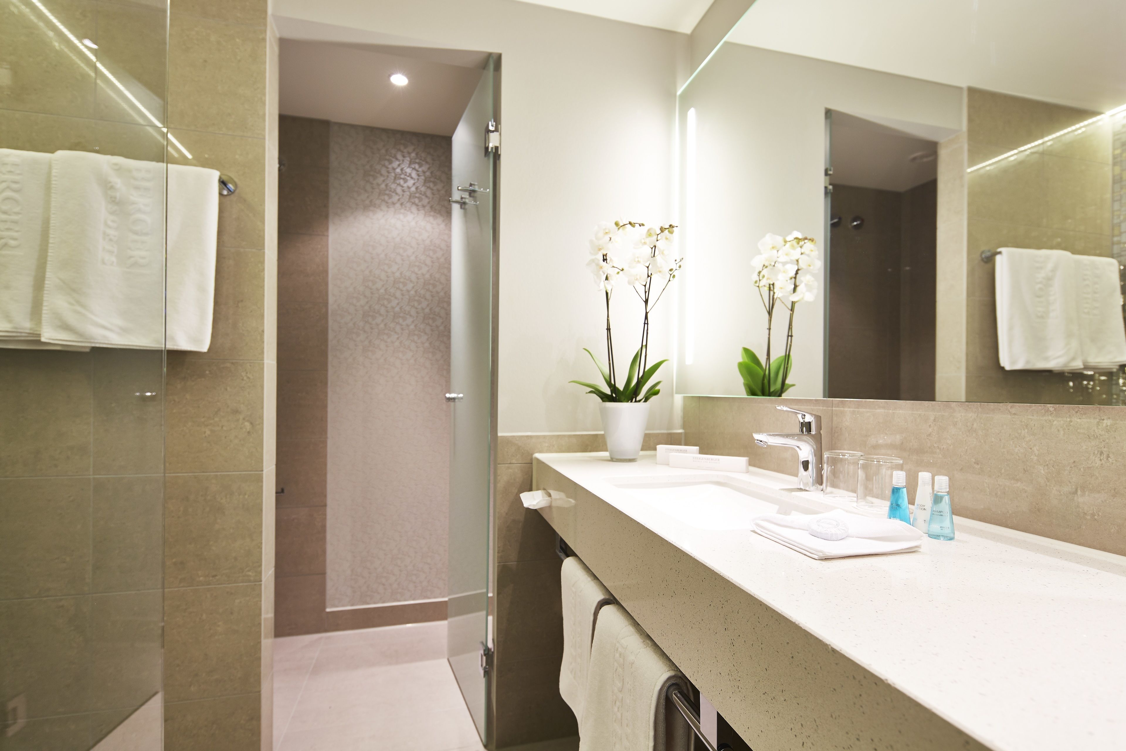 A modern bathroom with a large mirror, a sink, and a shower area.