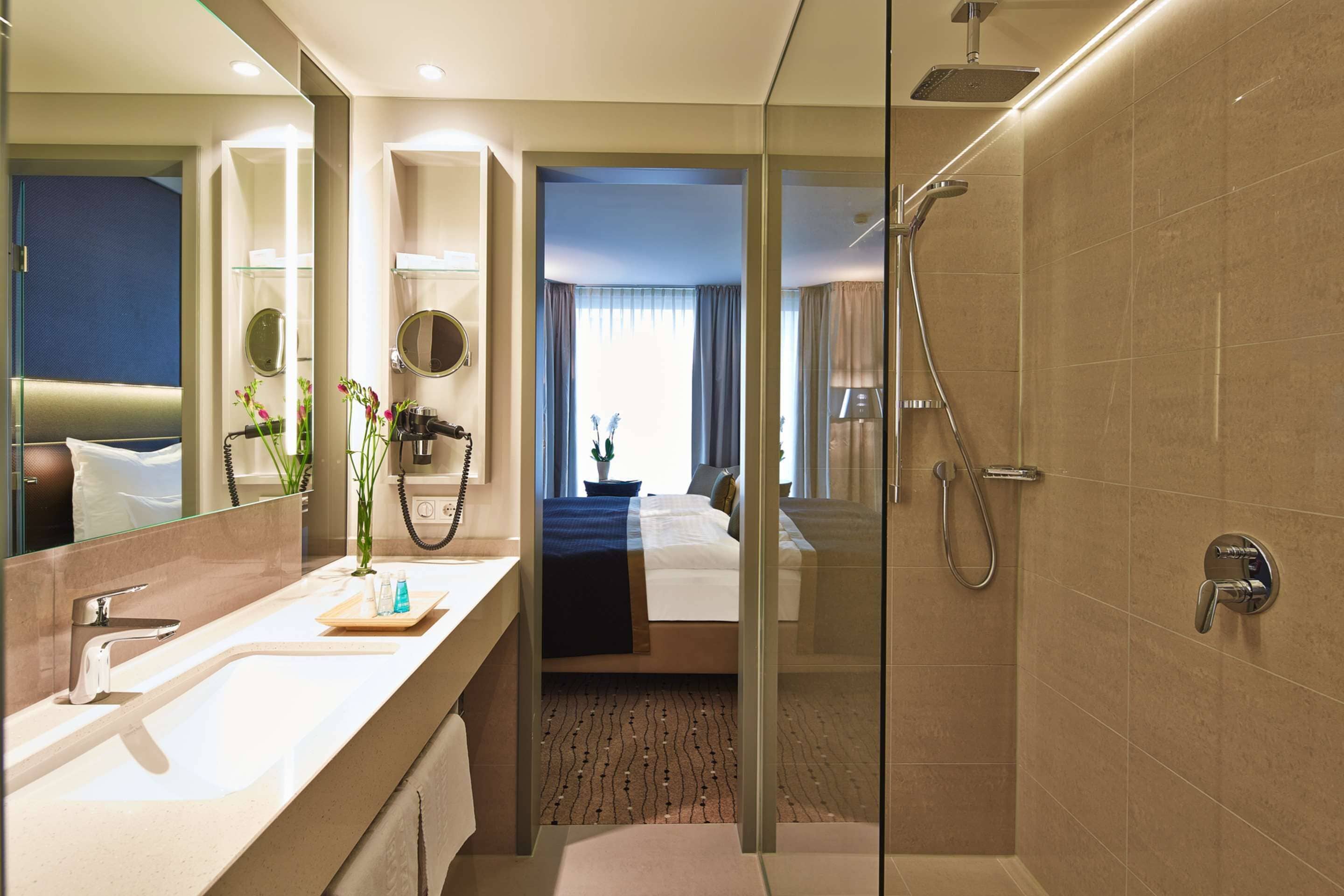 A modern hotel bathroom with a glass-enclosed shower, a large mirror, and a vanity with a sink and towel rack.