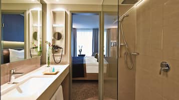 A modern hotel bathroom with a glass-enclosed shower, a large mirror, and a vanity with a sink and towel rack.