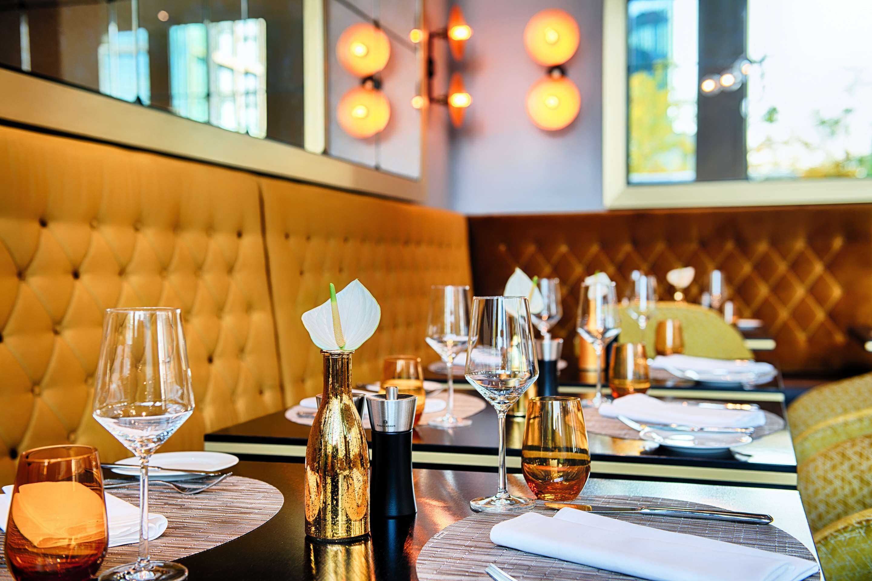 A restaurant setting with a tufted leather booth, dining tables set with wine glasses, plates, and cutlery.