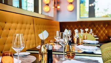 A restaurant setting with a tufted leather booth, dining tables set with wine glasses, plates, and cutlery.